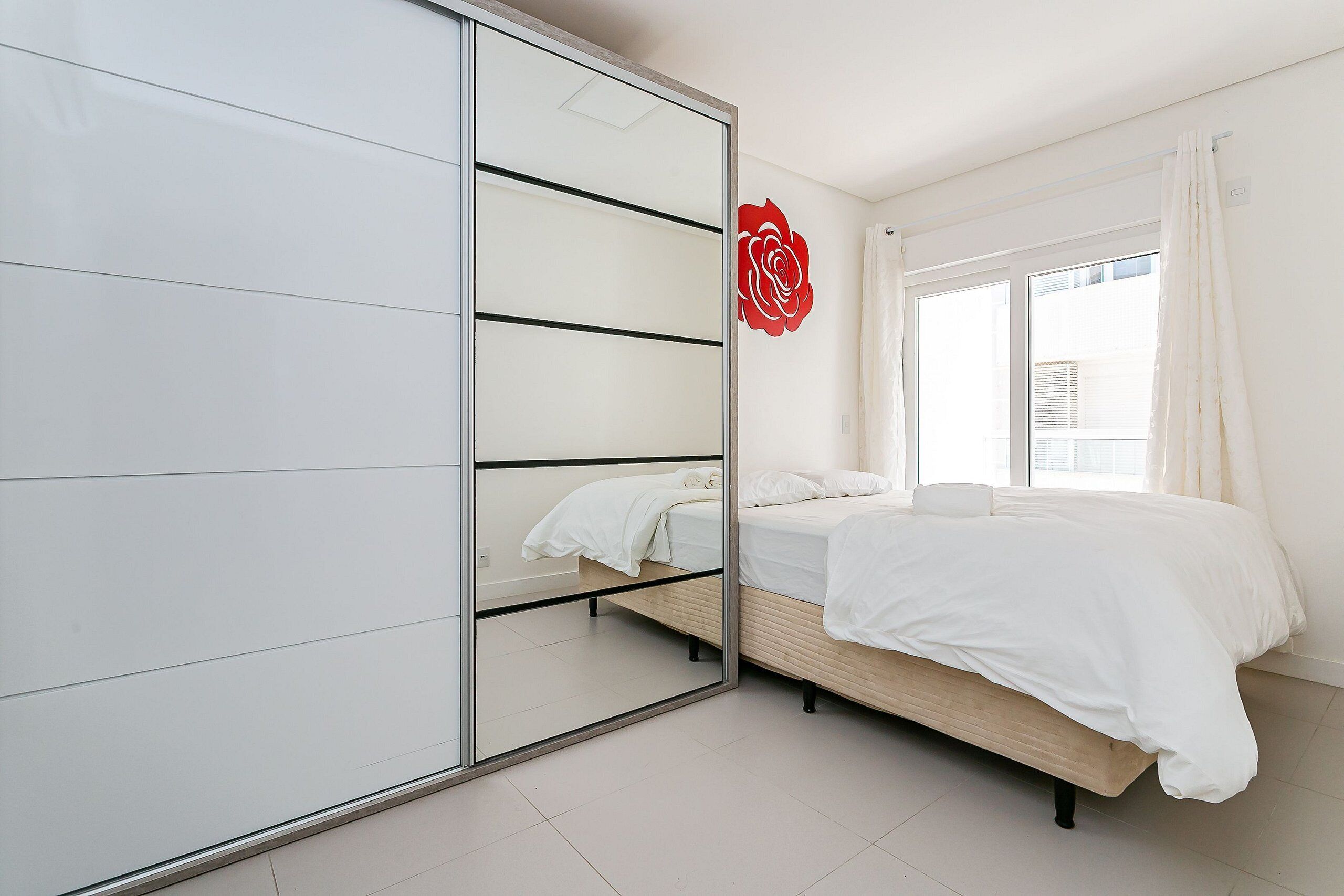 Un dormitorio con cama, armario, ventana con cortinas y una decoración de rosa roja.