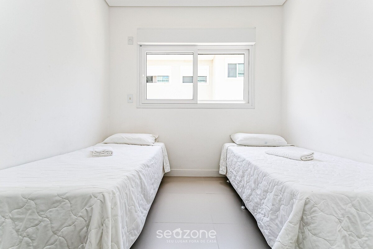 A small, clean room with two beds, a window, and a tiled floor.