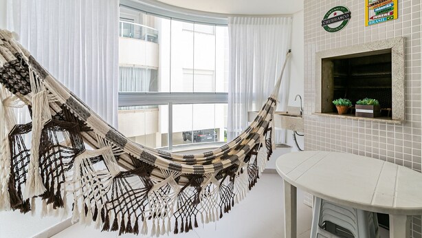 A hammock in a room with a view of a building outside. There is a tiled wall with a sign above it. - Apto em prédio c/ piscina 350m da praia RTG208 (Florianópolis)