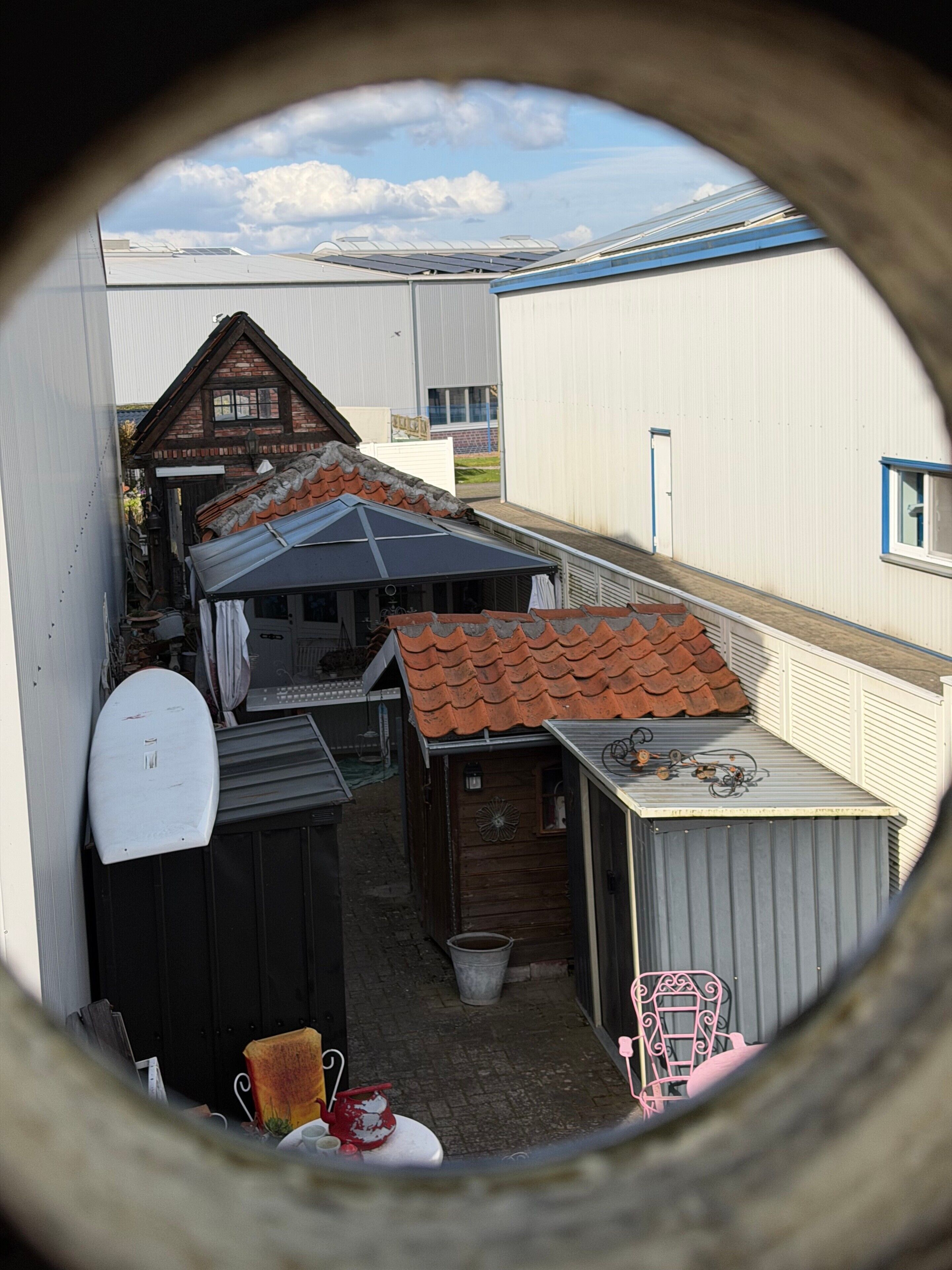 Ein schmaler Gang mit einem kleinen Holzhaus, einer Metallhütte und einem weißen Gebäude mit blauer Verzierung.