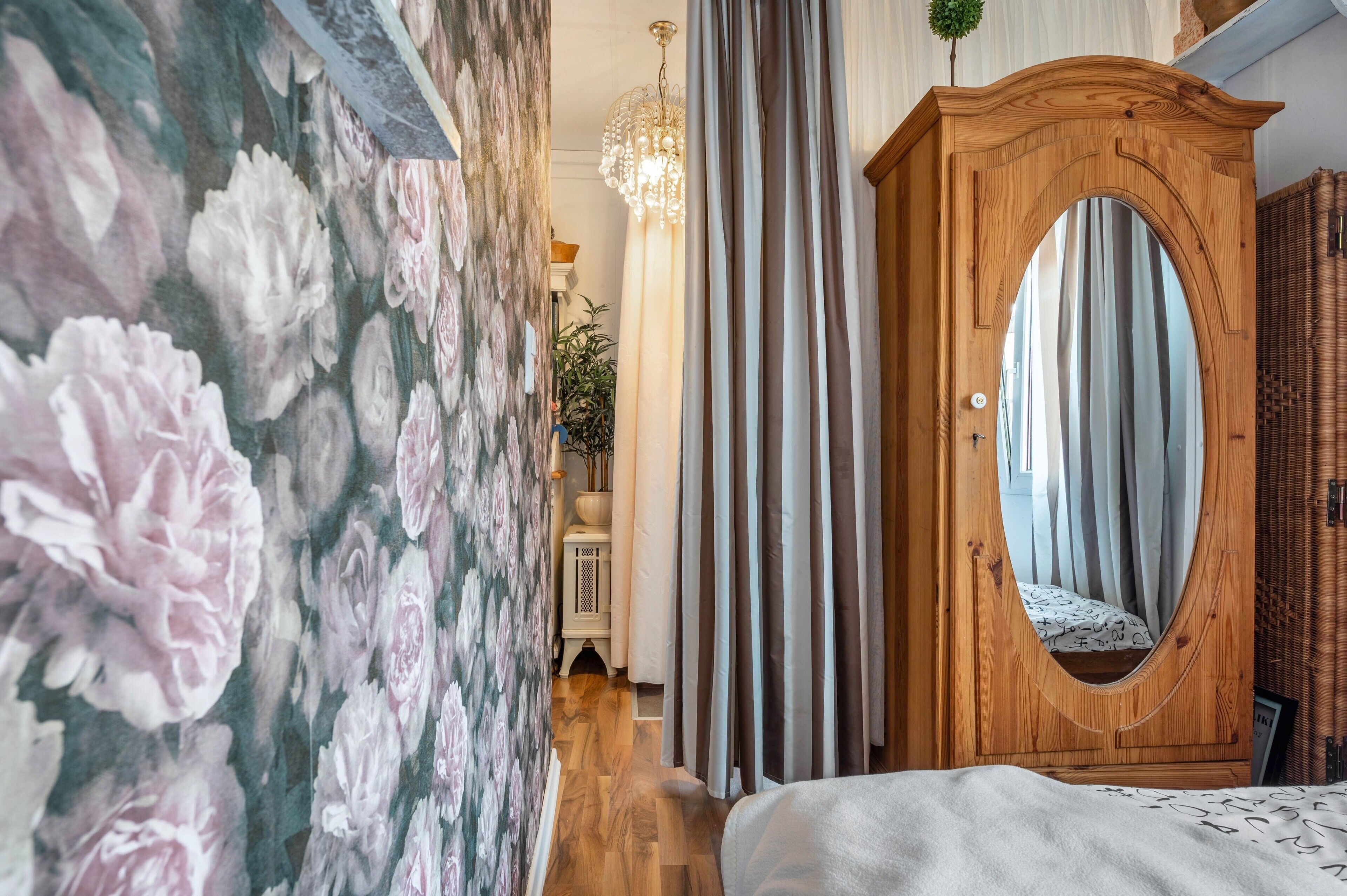 Ein Zimmer mit floralem Wandpapier, einem Holfischschrank mit Spiegel, einem Bett und einer Pendelleuchte.