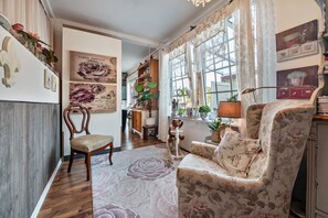 A cozy room with a wooden floor, a floral armchair, a wooden chair, a rug, and a bookshelf with decorative items. - Apartment 'Kleine Oase Stuhr im Container E G' with Shared Terrace, Garden & Wi-Fi (Stuhr-Brinkum)