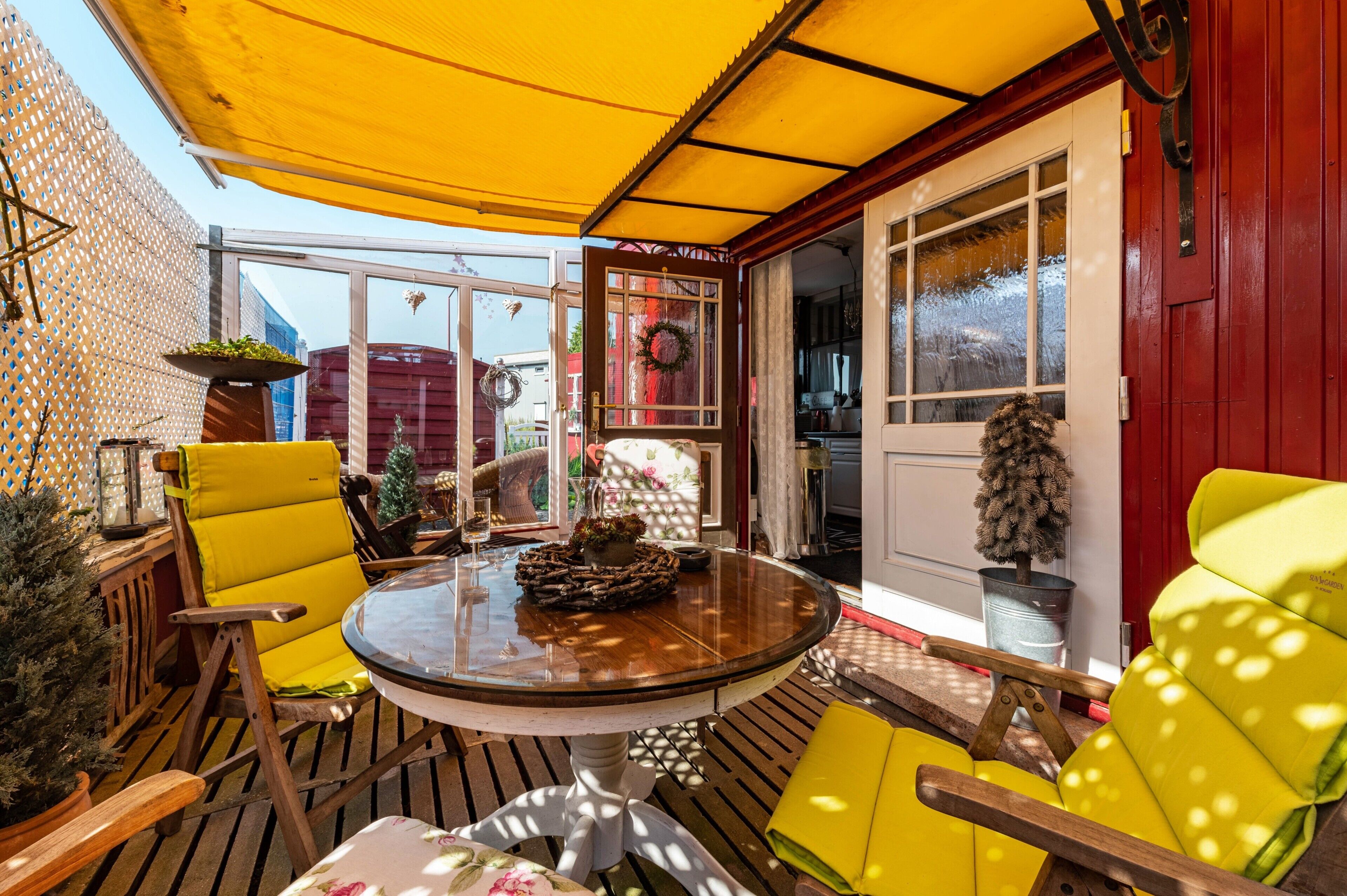 Un patio soleado con una mesa de madera, sillas amarillas y una planta en maceta.