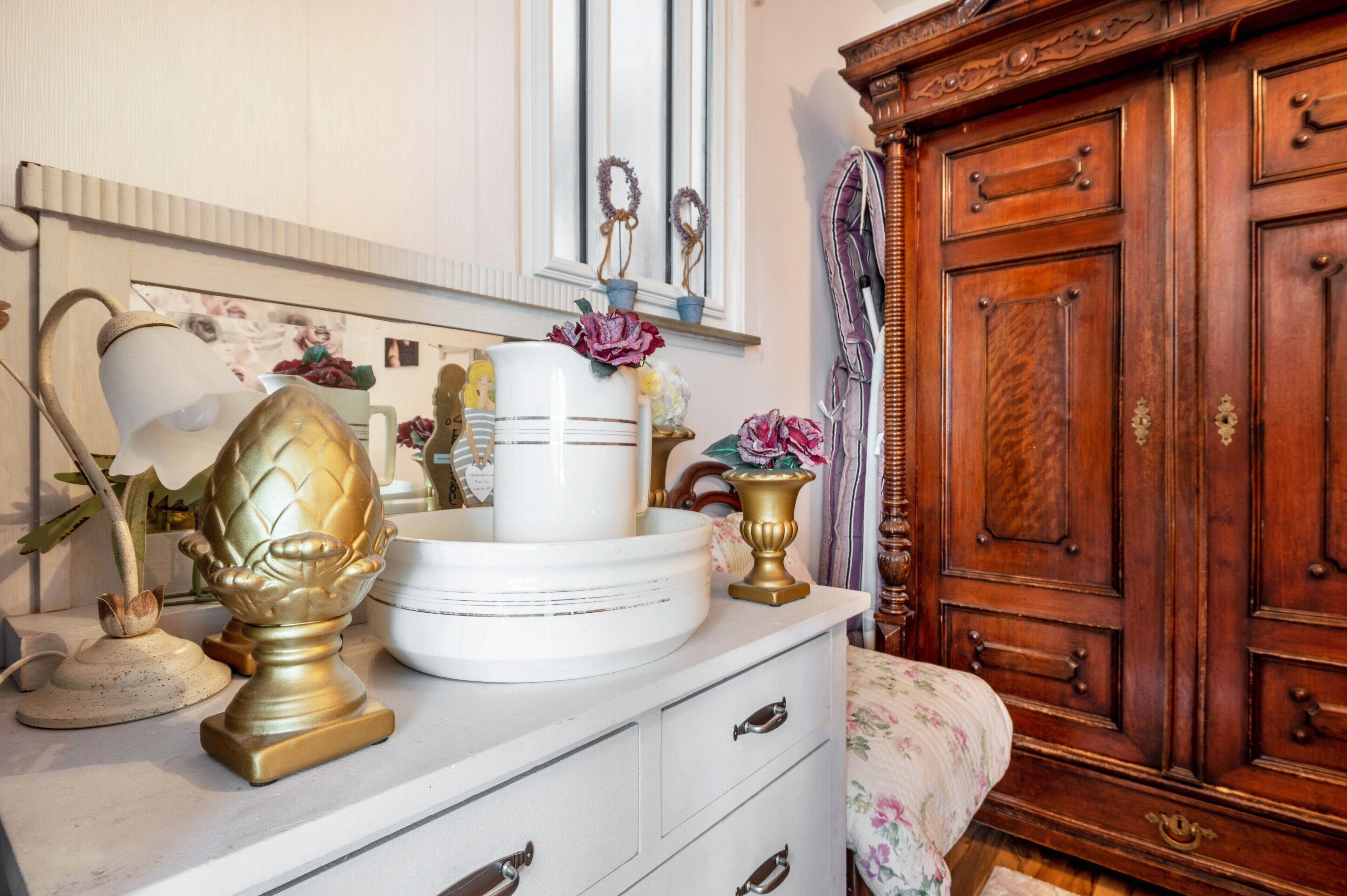 A room with a white dresser, a wooden cabinet, and decorative items including a vase and a lamp.