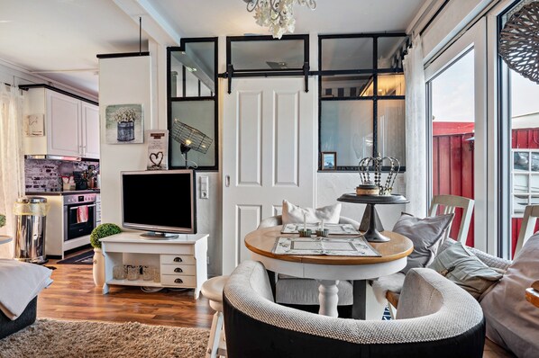 A modern kitchen with a flat-screen TV, a dining area with a round table, and a large window with a view.