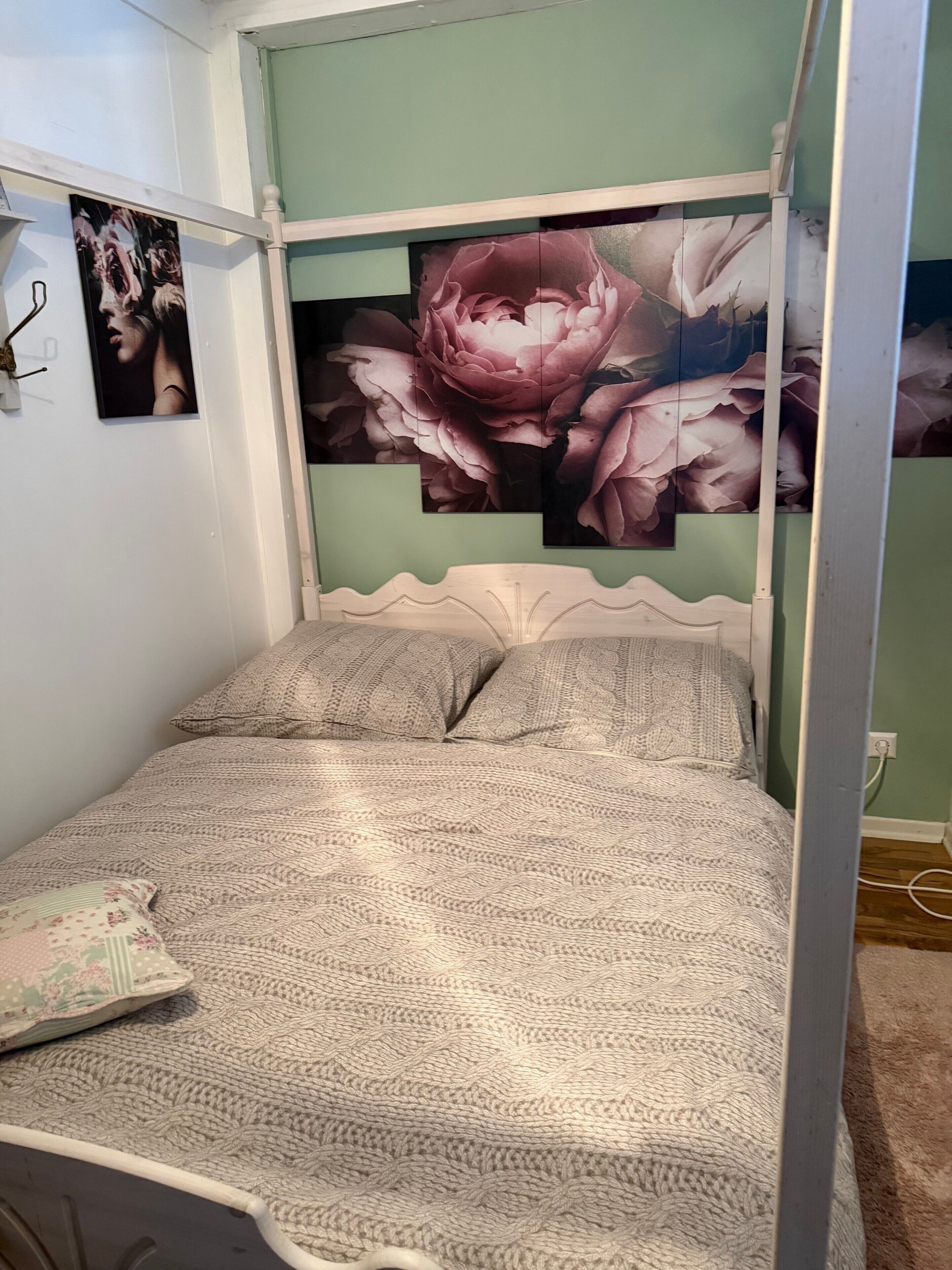 Ein Bett mit gemustertem Überwurf, einem Kopfteil und einer Wand mit einem Blumenbild.