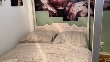 Ein Bett mit gemustertem Überwurf, einem Kopfteil und einer Wand mit einem Blumenbild.