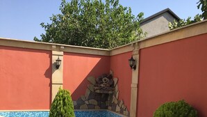 A pool area with a tiled edge, a stone wall, and a wooden table and chair. - 3 storey Villa (Baku)