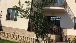 A multi-story building with a balcony, a small garden area with a tree, and a paved entrance. - 3 storey Villa (Baku)