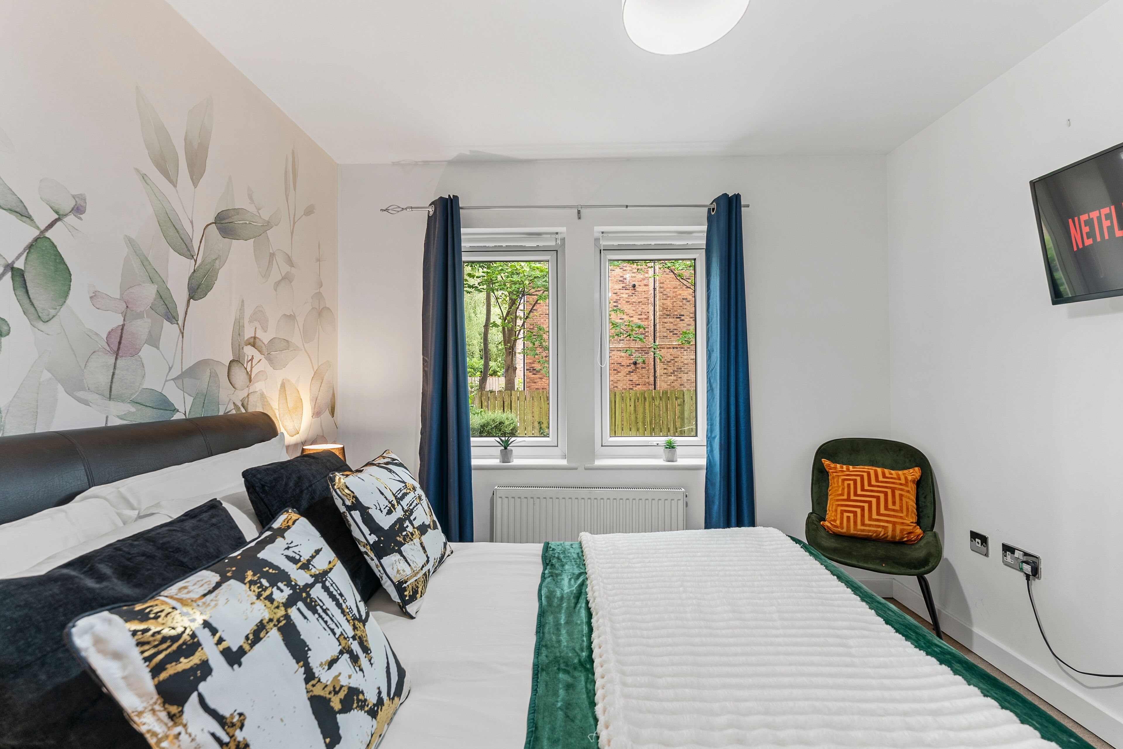 A bedroom with a bed, a chair, a TV, and a window with curtains.