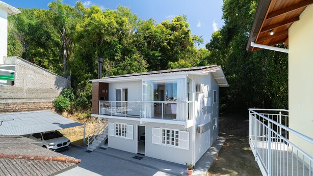 A two-story house with a balcony, a car parked in front, and a garden area.