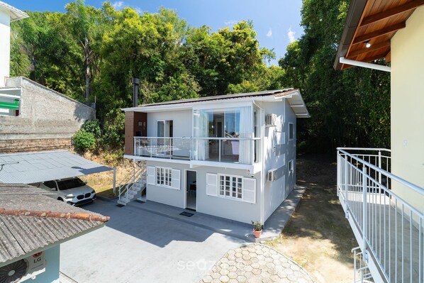 A two-story house with a balcony, a car parked in front, and a garden area. - Aptos a 2min da Praia de Canasvieiras Floripa-sc RTB (Florianópolis)