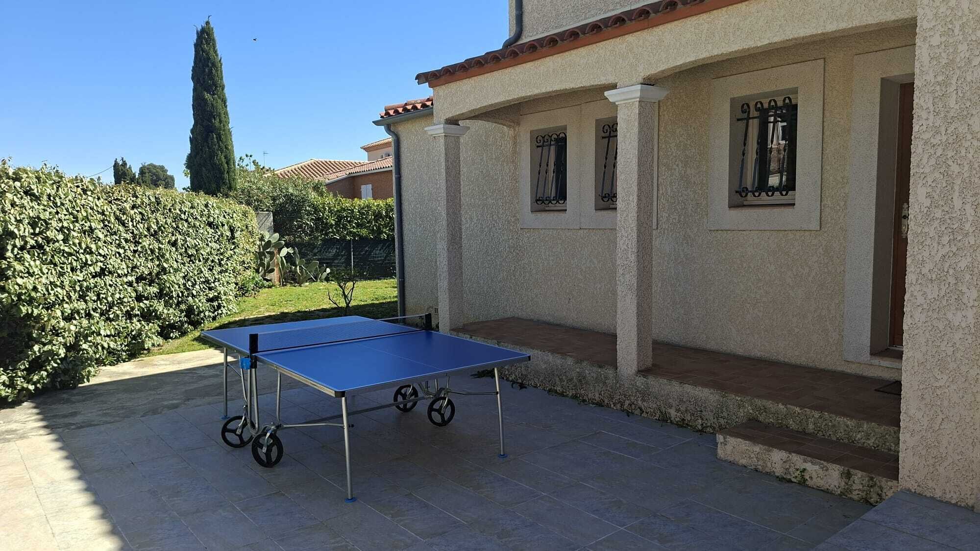 A ping pong table in an outdoor patio area with a house in the background.