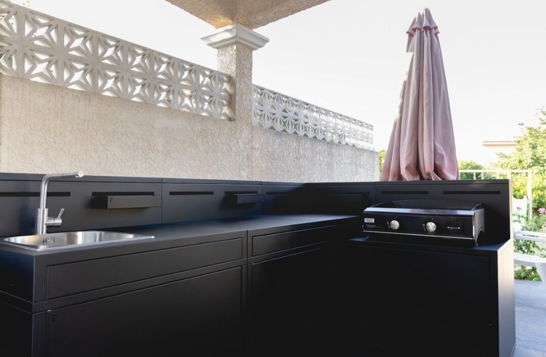 A modern outdoor kitchen with a built-in grill, a sink, and a decorative white lattice wall.