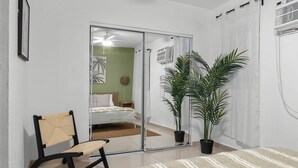 Un dormitorio con una cama, una silla, un espejo grande y dos plantas en macetas.