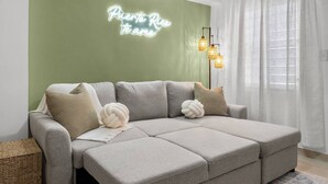 Una sala de estar moderna con un sofá seccional grisáceo, un letrero de neón en la pared y una lámpara de pie.
