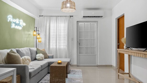 Una sala moderna con un sofá gris, una mesa de centro de mimbre y un televisor de pantalla plana sobre un soporte de madera.