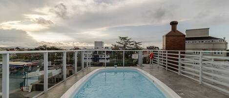 An indoor swimming pool with a view of the cityscape and a cloudy sky.