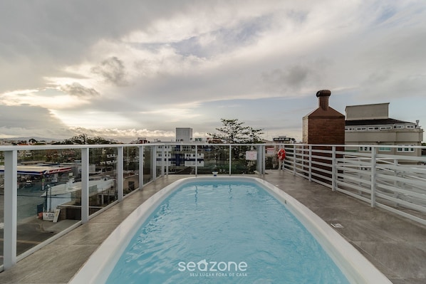 An indoor swimming pool with a view of the cityscape and a cloudy sky.