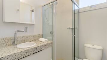 Un baño moderno con ducha de vidrio, lavamanos con encimera de granito y un inodoro blanco.