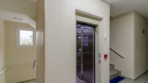 Un ascenseur situé dans un couloir, avec une fenêtre, une main courante et un détecteur d’incendie.