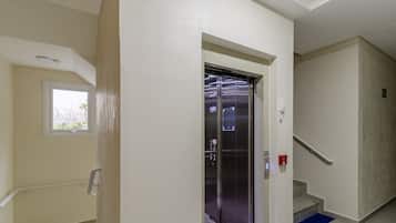 Un ascensor en un pasillo con ventana, barandilla y detector de incendios.
