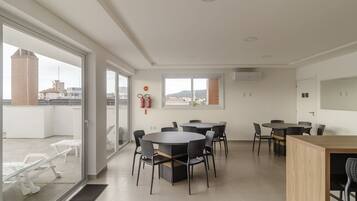Una habitación de hotel moderna con un amplio ventanal corredero que da a un balcón, una mesa de comedor redonda con sillas y una pequeña zona de kitchenette.