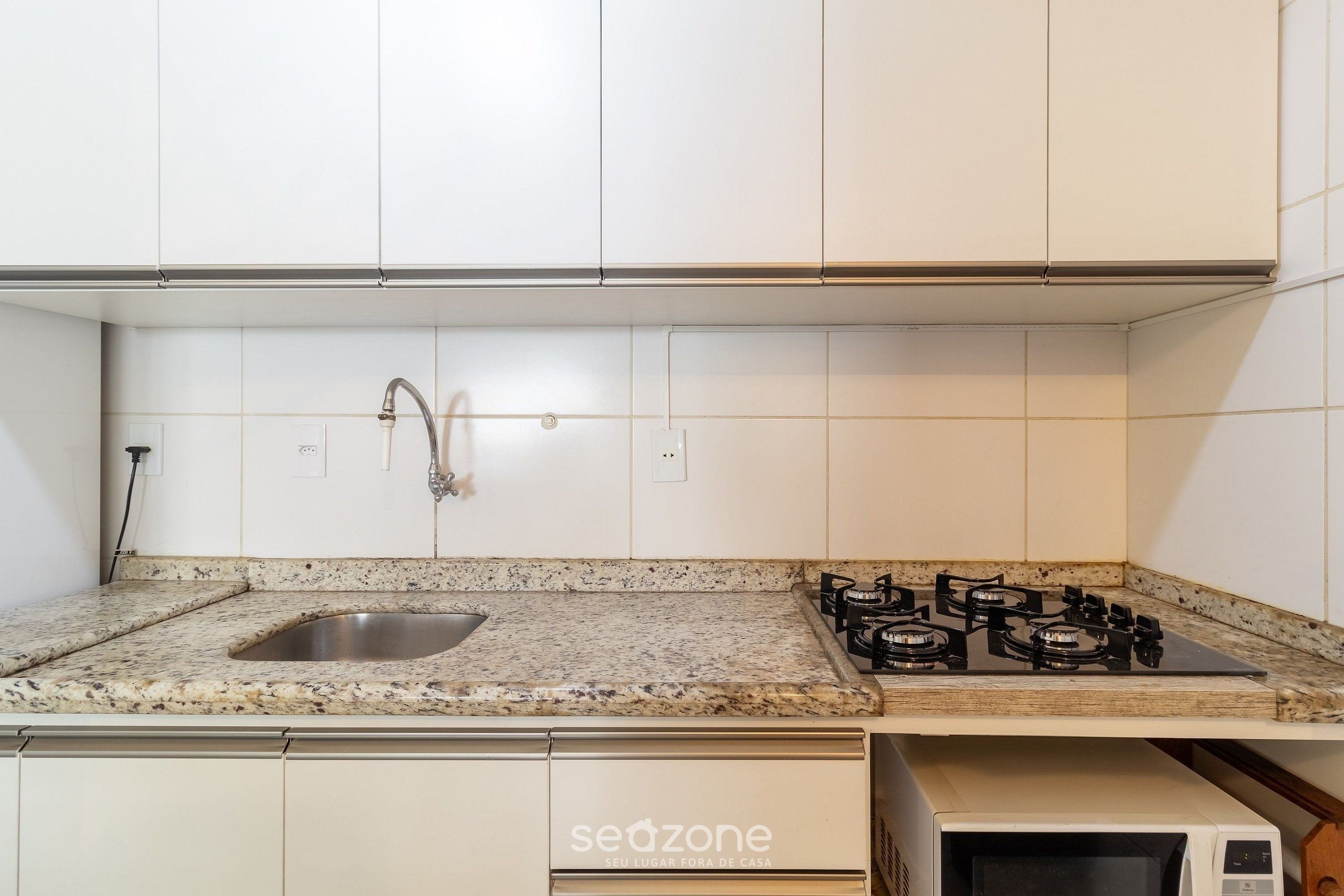Una cocina con gabinetes blancos, encimera de granito, pileta de acero inoxidable, cocina a gas y microondas.