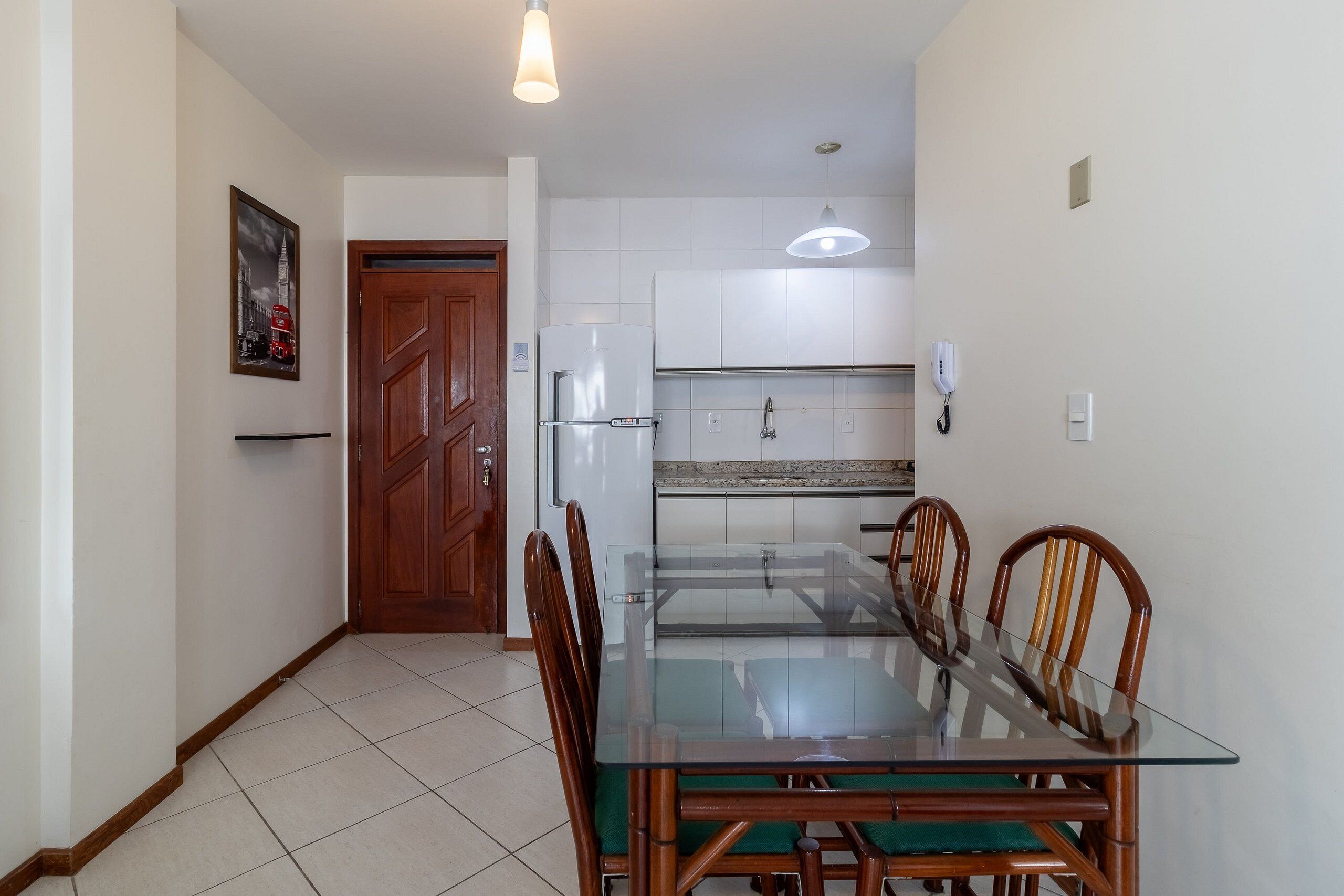 A dining area with a glass table and wooden chairs, a wooden door, and a kitchen with white cabinets and a tiled backsplash.