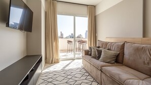A modern living room with a sofa, a flat-screen TV, a sliding glass door leading to an outdoor area with chairs. - Apartment in the Center With Pool Rri103 (Florianópolis)