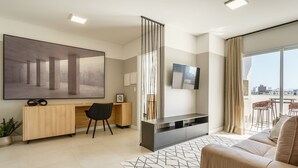 A modern living room with a large flat-screen TV, a sofa, a desk with a chair, and a large abstract painting. - Apartment in the Center With Pool Rri103 (Florianópolis)
