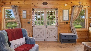 A cabin interior with a wooden ceiling, a couch with a 'Welcome Home' pillow, a bench, and a door with a 'Cabin Rules' sign. - The Nest-A Cozy Rustic Escape for Two (Fredericksburg)