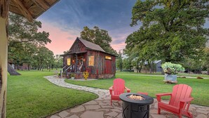 A rustic wooden cabin with a stone pathway leading to a fire pit and red Adirondack chairs. - The Nest-A Cozy Rustic Escape for Two (Fredericksburg)