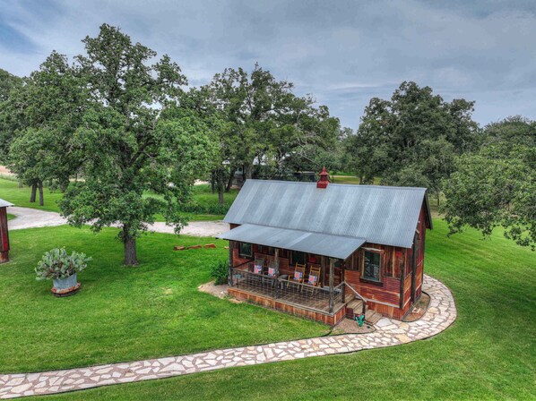 A rustic cabin with a porch, surrounded by lush greenery and trees.