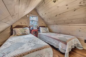 Um quarto de sótão acolhedor com duas camas, uma mesa pequena e um vitral.