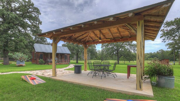 Un patio techado con mobiliario exterior, una estructura de madera y un sendero de piedra.