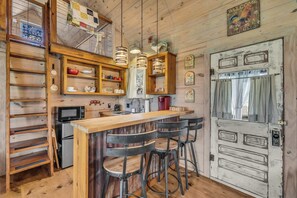A rustic kitchen with wooden shelves, a wooden bar counter, and bar stools.