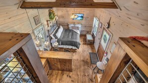 Acogedora habitación tipo cabaña con cama en altillo, paredes de madera, chimenea y televisor.