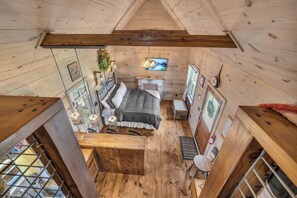 A cozy cabin-style room with a loft bed, wooden walls, a fireplace, and a television. - The Roost - Charming Hill Country Hideaway (Fredericksburg)