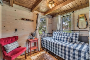A cozy cabin room with a bed, a red chair, a small table, and a mirror on the wall.