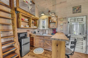 A rustic kitchen with wooden shelves, a refrigerator, a microwave, and a coffee maker.