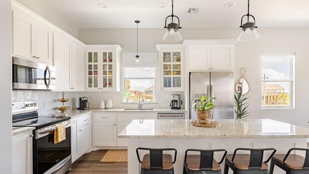 Una cocina moderna con armarios blancos, electrodomésticos de acero inoxidable y una isla central con taburetes de bar.