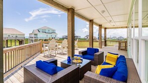 Una terraza techada al aire libre con mobiliario de mimbre y vista a casas al fondo.