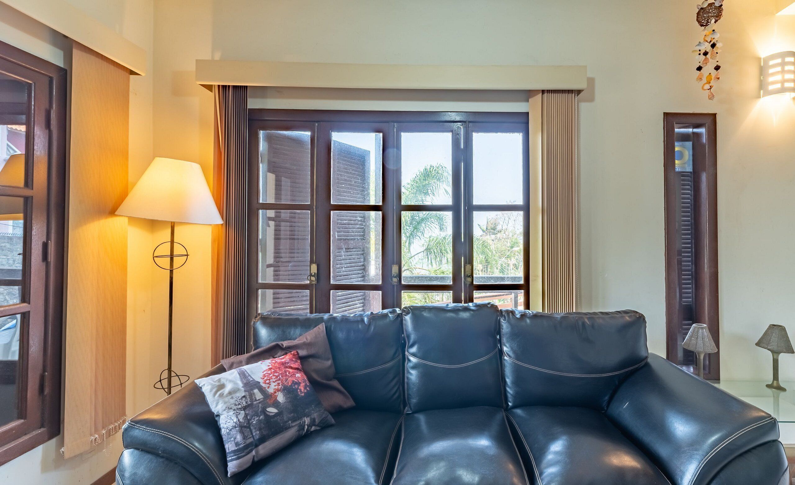 A black leather sofa with a decorative pillow, a floor lamp, and a window with curtains.