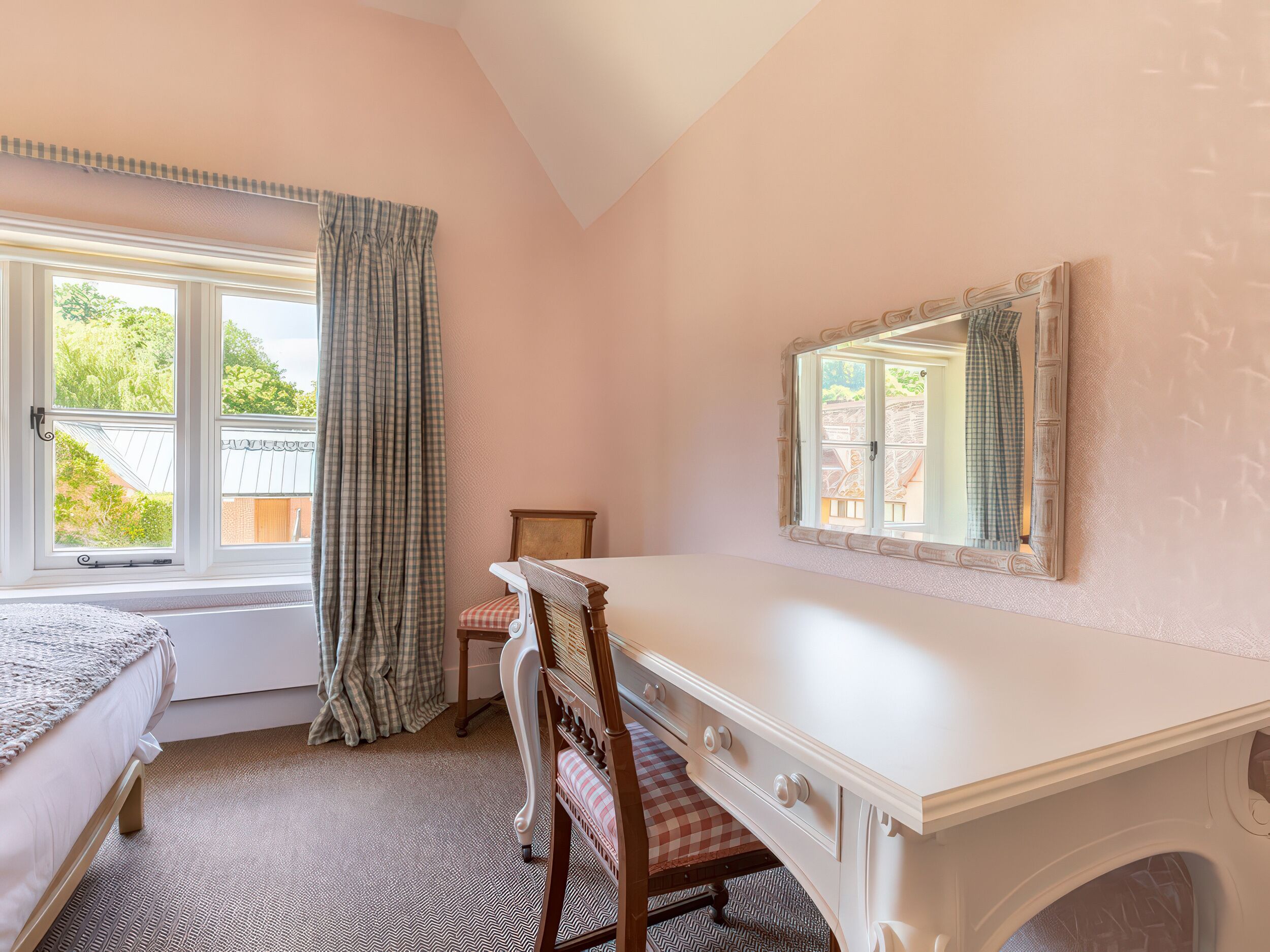 A bedroom with a bed, a desk, a chair, a window with curtains, and a mirror.