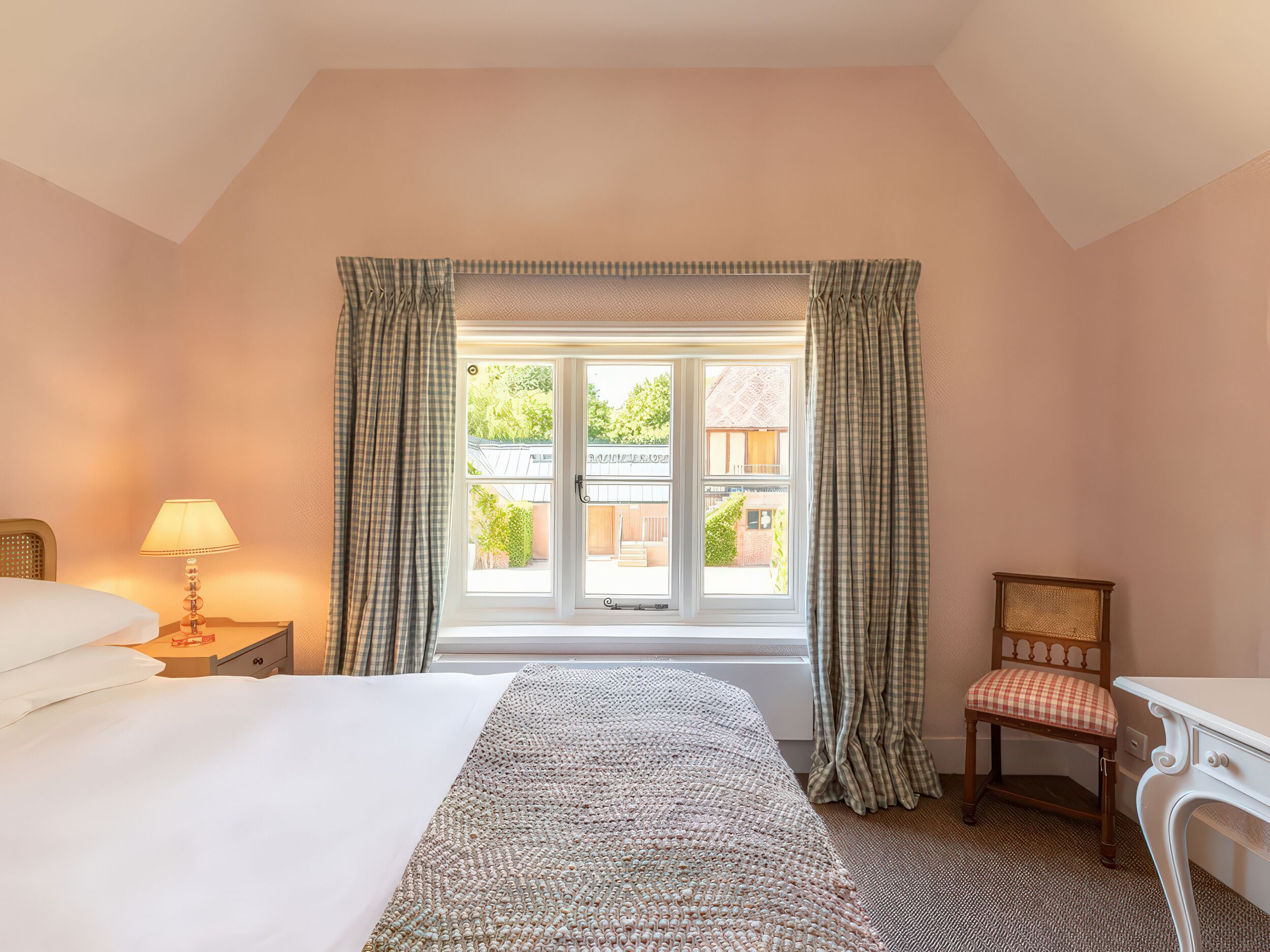 A bedroom with a bed, a desk, a chair, a lamp, and a window with curtains.