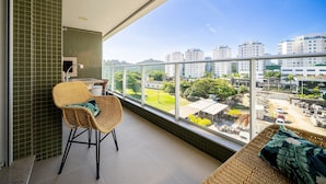 A balcony with a wicker chair, a cushioned bench, and a view of a cityscape with buildings and greenery. - Charming apt w/ Balcony 150m From the Beach Abc0403 (Itajai)