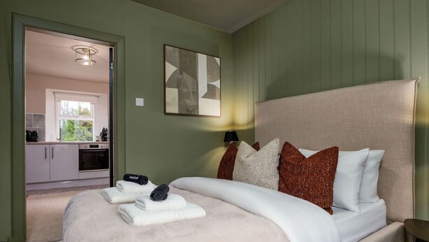 Une chambre à coucher avec un lit, des oreillers et une table de chevet. Il y a une fenêtre et une porte qui donne sur une salle de bain.