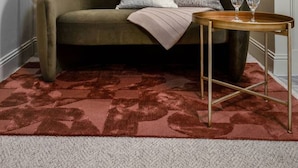 Un salon avec un canapé vert, un tapis rouge à motifs, une petite table avec deux verres, une plante en pot et, au mur, un tableau abstrait moderne.