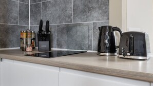 A kitchen with a black induction cooktop, a kettle, and a toaster. There are also spice containers and a knife set on the counter.